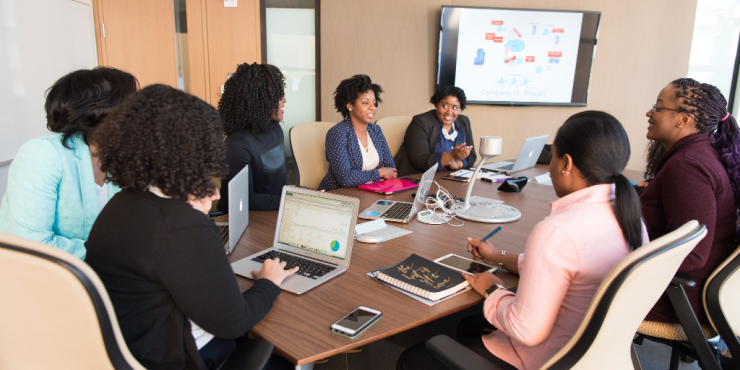 Professional women in a meeting, discussing 'Company vs. Threats' on a screen, showcasing an AI-Powered Creative Process.